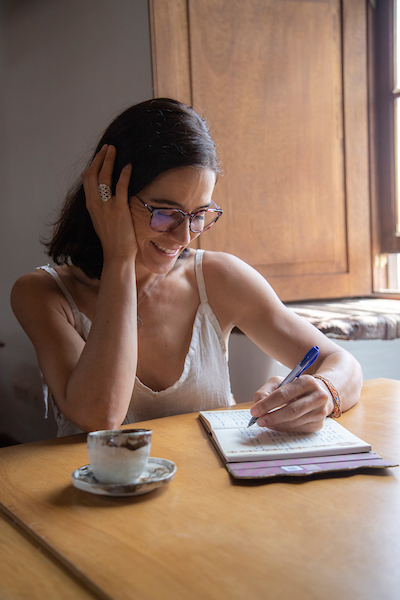 Itziar Goikolea escribiendo en su cuaderno junto a una taza de té, en un espacio íntimo y sereno.